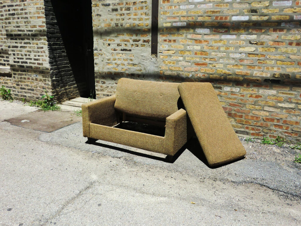 Abandoned armchair on footpath against building during sunny day