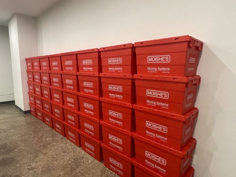 Stack of bright red plastic moving boxes labeled Moishe's Moving Systems