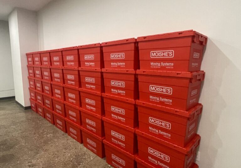 Stack of bright red plastic moving boxes labeled Moishe's Moving Systems